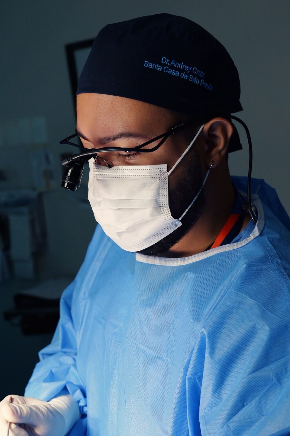 Dr. Andrey Cruz em centro cirúrgico, usando touca, máscara e lupa cirúrgica